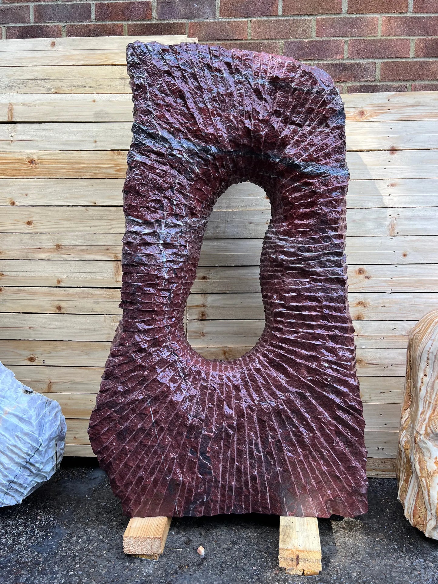 Unique sculpture garden monolith resembling flamingo hues, blending beautifully with garden stones and pebbles.