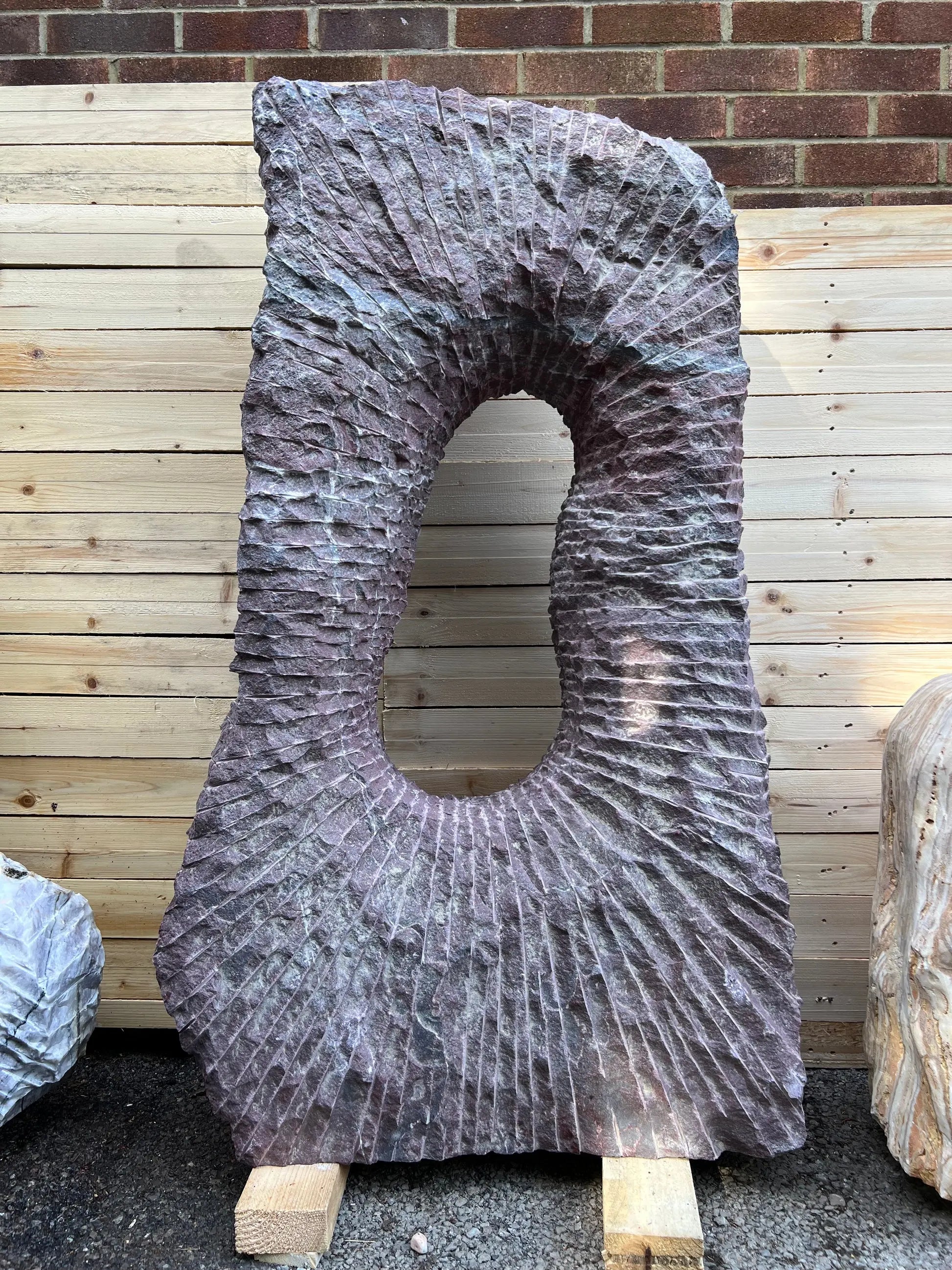 dark red natural stone monolith on a wooden base, perfect for landscaped gardens or gravel areas.