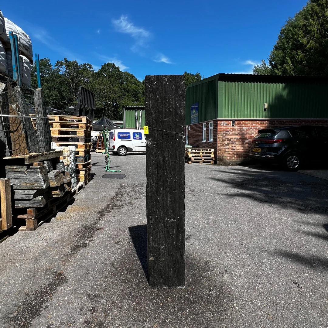 Dark textured stone monolith displayed outdoors, creating a dramatic unique piece among garden pebbles and gravel.