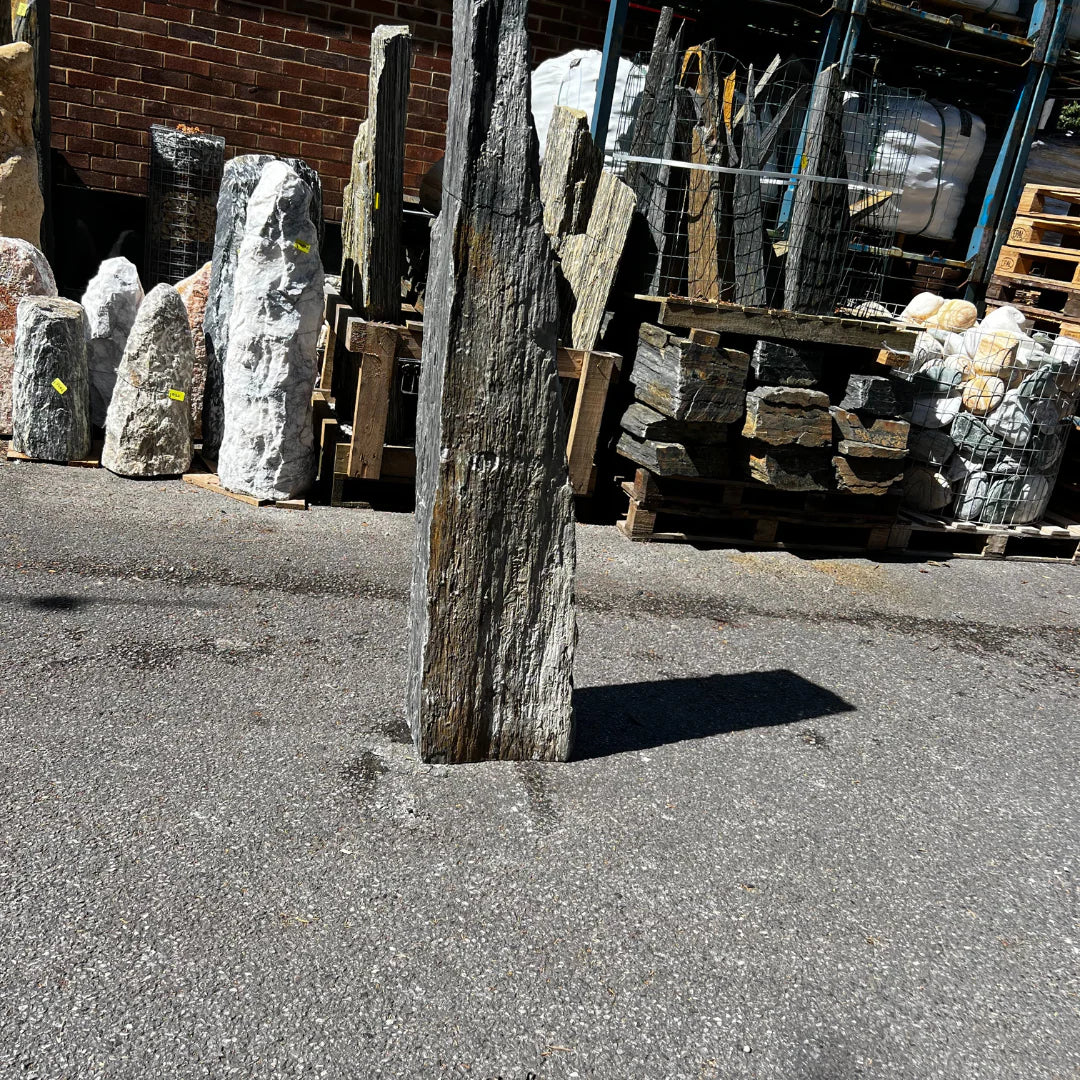 Tall natural stone monolith with a rugged texture displayed outdoors on a concrete surface, surrounded by other decorative garden stones.