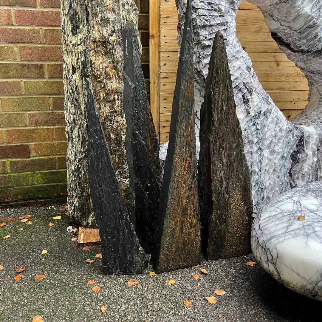 Pack of five mini natural stone shale monoliths with pointed tops in dark brown and black tones, displayed outdoors beside larger decorative stones at Stones4Gardens.